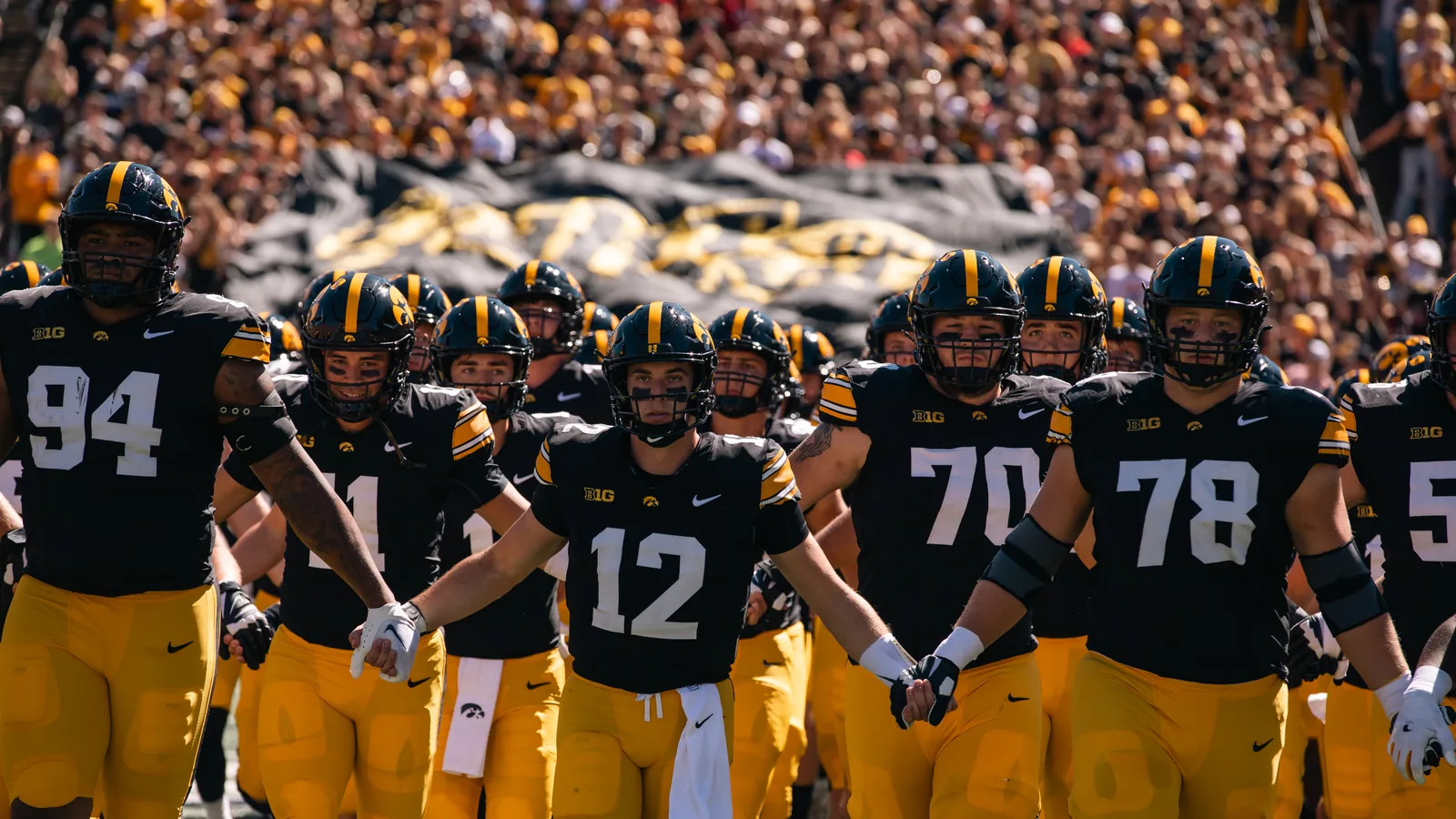 Iowa football players in black-and-gold uniforms take the field at Kinnick Stadium.