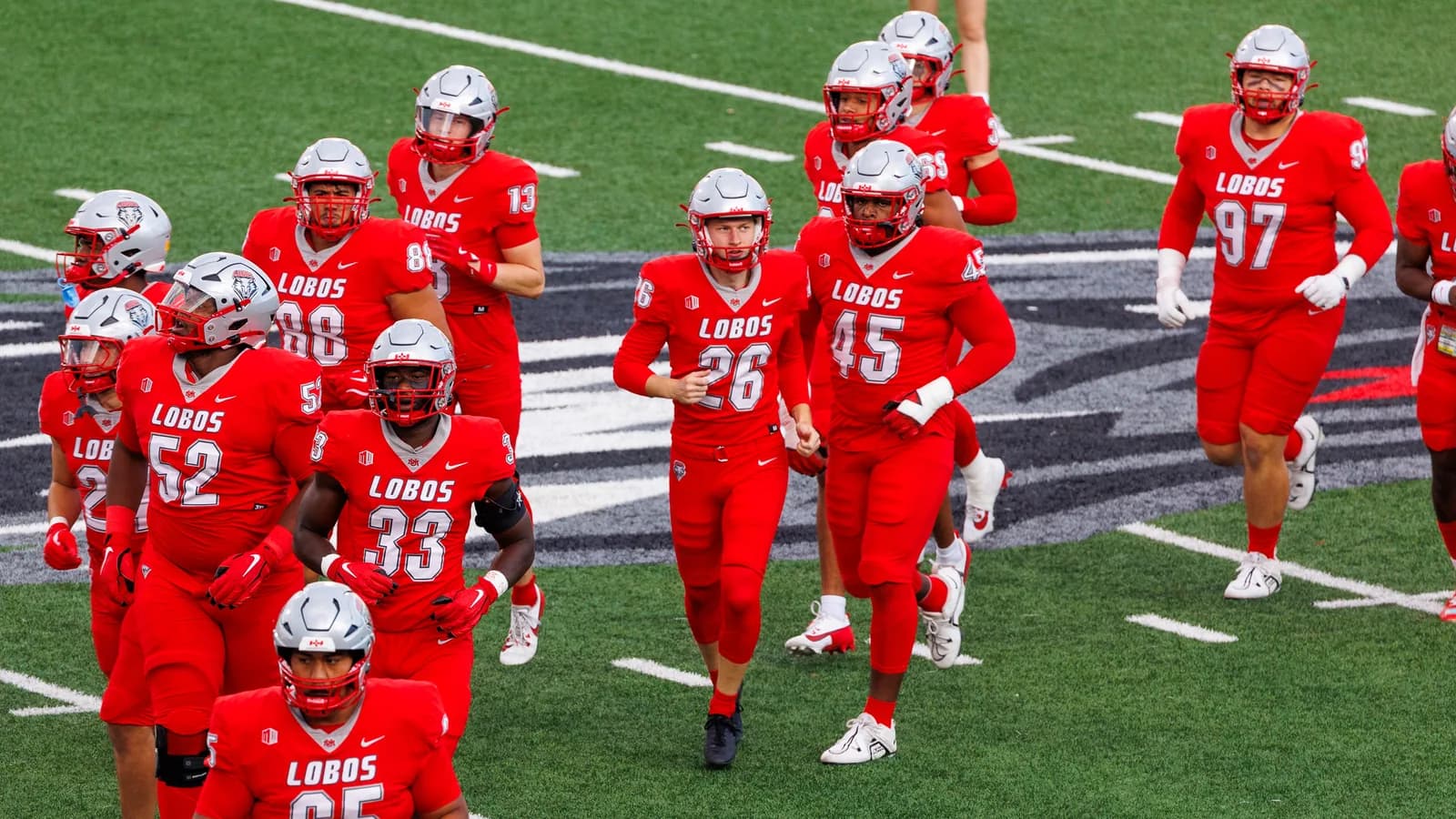 New Mexico players in red Lobos uniforms take the field in 2024.